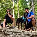 Smile, Dog, Plant, Tree, Dog breed, Carnivore, Sunglasses, Leisure, Bedrock, Goggles, Recreation, Forest, Fun, Trail, Jungle, Luggage And Bags, Wilderness, Backpack, Shorts, Adventure